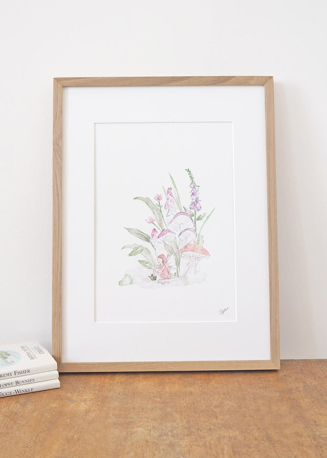 Framed Art print of a little fairy sitting under magical mushrooms and pink flowers, painted by Carla Gebhard.