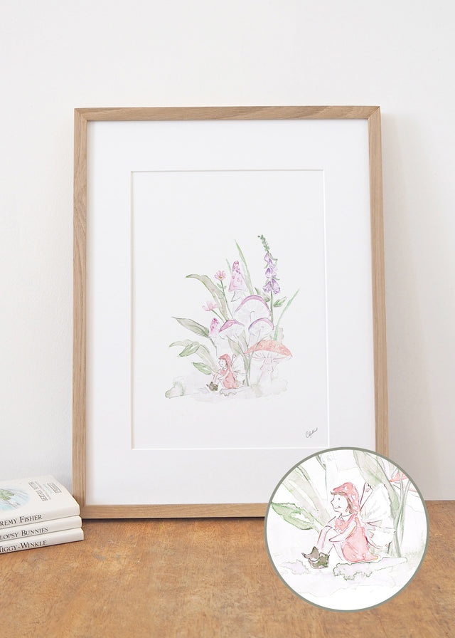 Framed Art print of a little fairy sitting under magical mushrooms and pink flowers, painted by Carla Gebhard.